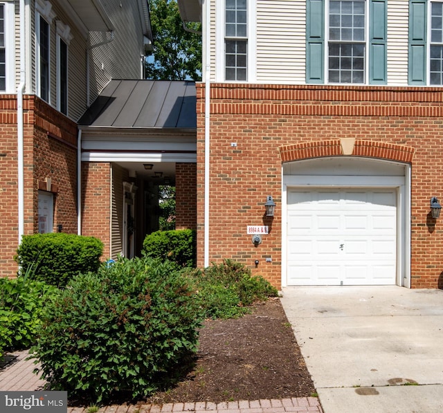 view of property exterior featuring concrete driveway, brick siding, an attached garage, and a standing seam roof