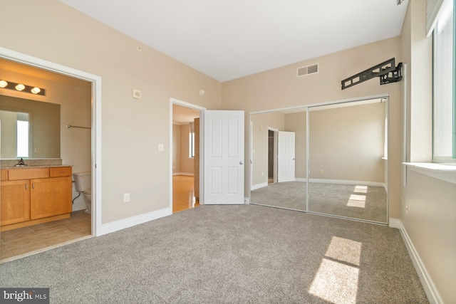 unfurnished bedroom featuring light carpet, a closet, ensuite bathroom, and baseboards