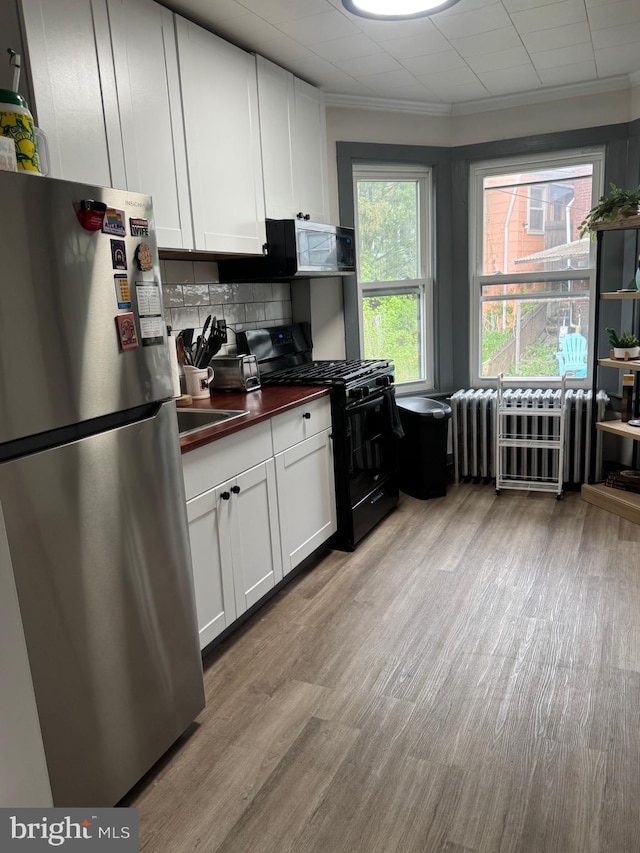 907 Birch St, Reading, PA 19604 - kitchen featuring appliances with stainless steel finishes, white cabinets, backsplash, light wood finished floors, and crown molding