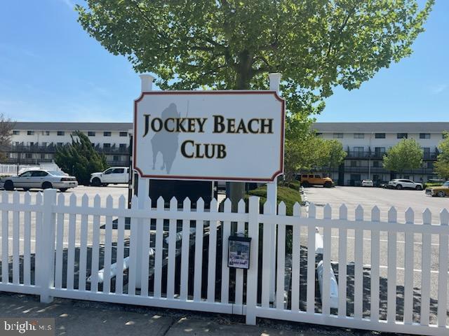 community sign with fence and uncovered parking
