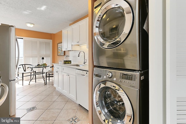 laundry room featuring laundry area, stacked washer / drying machine, a textured ceiling, a sink, and light tile patterned floors