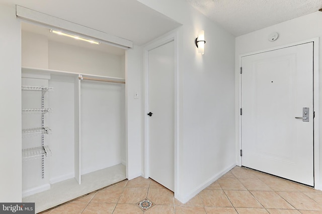 interior space featuring a textured ceiling, baseboards, and light tile patterned flooring