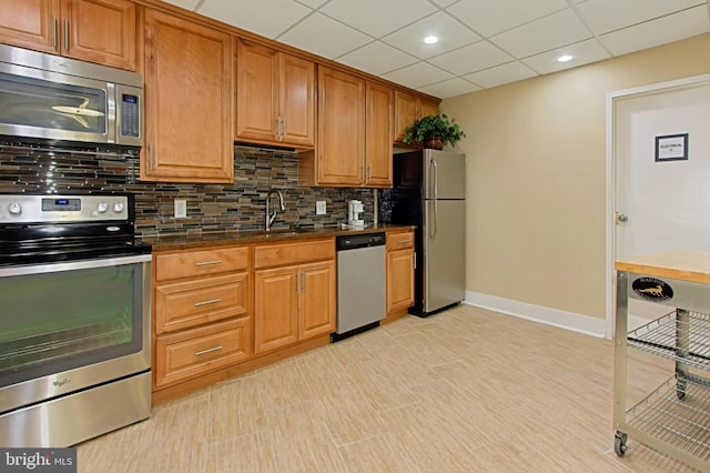 kitchen with dark countertops, a sink, stainless steel appliances, baseboards, and tasteful backsplash