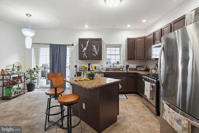 kitchen featuring dark brown cabinetry, a kitchen island, a breakfast bar area, stone counters, and stainless steel appliances