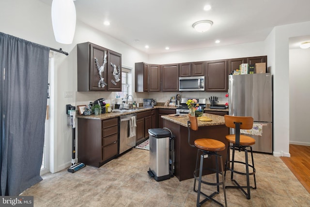 kitchen with dark brown cabinetry, appliances with stainless steel finishes, a sink, a breakfast bar area, and a center island
