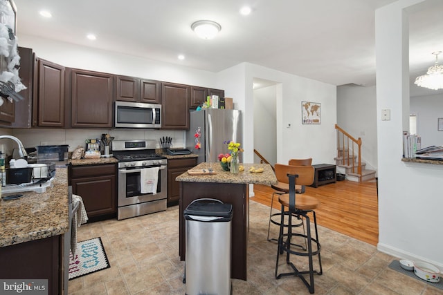 kitchen featuring dark brown cabinetry, light stone countertops, a kitchen breakfast bar, stainless steel appliances, and a kitchen island