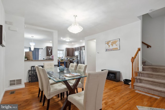 dining area featuring visible vents, light wood-style floors, a chandelier, and stairway