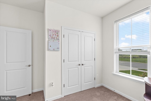 unfurnished bedroom featuring carpet flooring, multiple windows, a closet, and baseboards