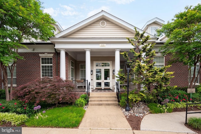 view of front facade with covered porch, brick siding, and french doors