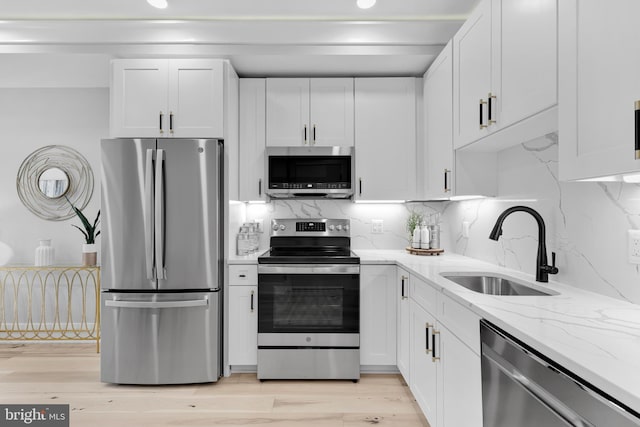 kitchen with light stone countertops, appliances with stainless steel finishes, a sink, white cabinetry, and decorative backsplash