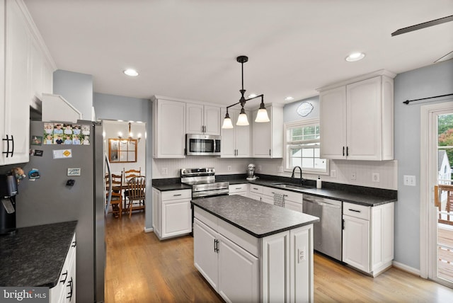 kitchen with appliances with stainless steel finishes, dark countertops, white cabinetry, a sink, and light wood-style flooring