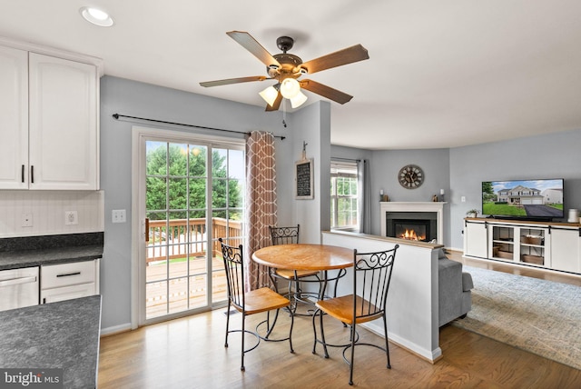 dining space featuring a glass covered fireplace, light wood-style flooring, a ceiling fan, baseboards, and recessed lighting