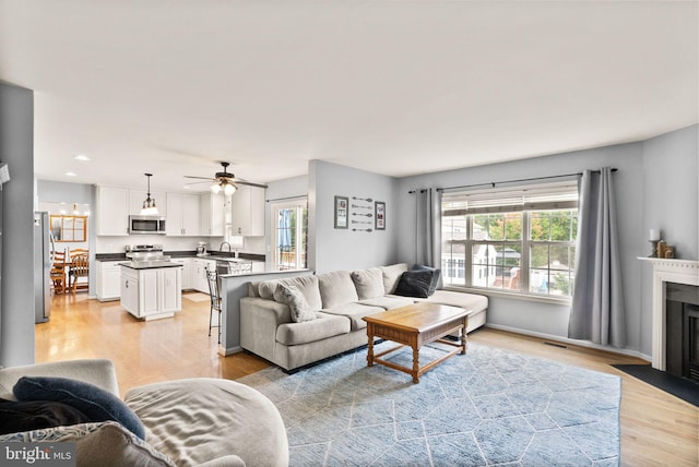 living area with recessed lighting, a fireplace with flush hearth, light wood-style flooring, and ceiling fan