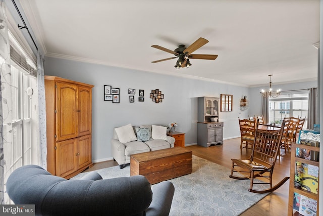 living area with crown molding, baseboards, light wood-style flooring, and ceiling fan with notable chandelier