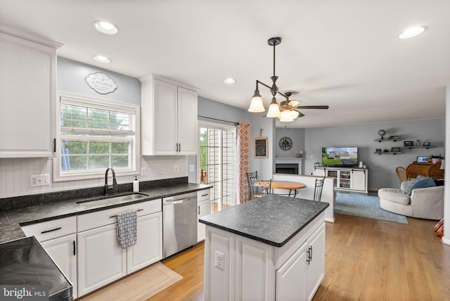 kitchen featuring white cabinets, dark countertops, a sink, dishwasher, and open floor plan