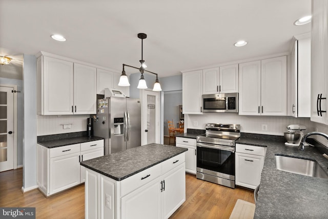 kitchen with dark countertops, light wood-type flooring, white cabinetry, a sink, and stainless steel appliances