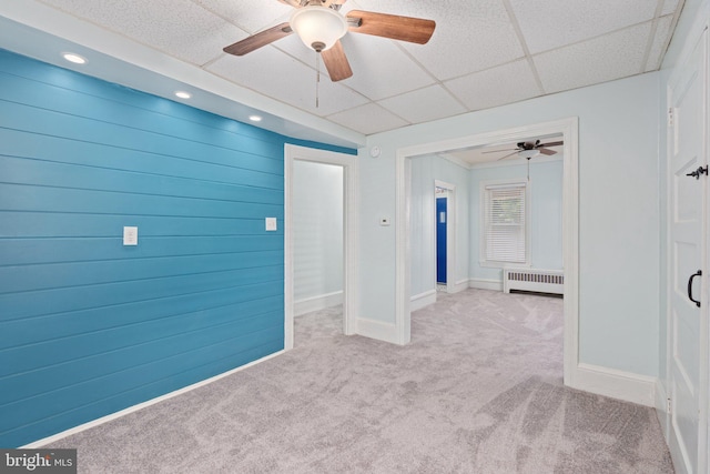 carpeted spare room featuring radiator heating unit, ceiling fan, baseboards, and a paneled ceiling