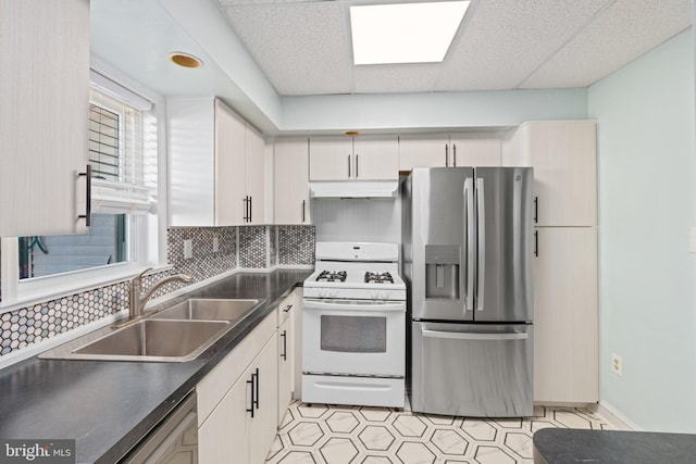 kitchen featuring stainless steel appliances, under cabinet range hood, a sink, dark countertops, and tasteful backsplash