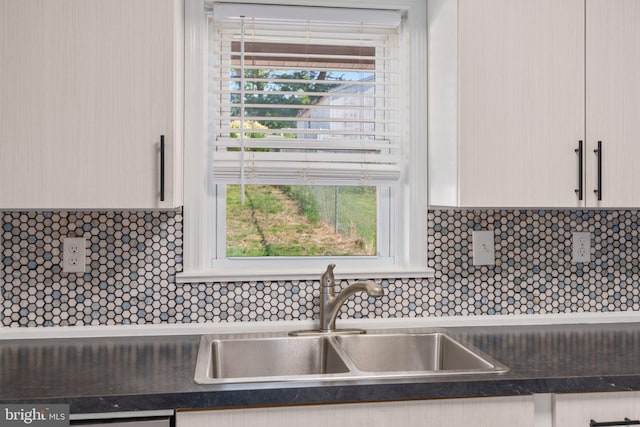 kitchen view of a sink, dark countertops, and decorative backsplash