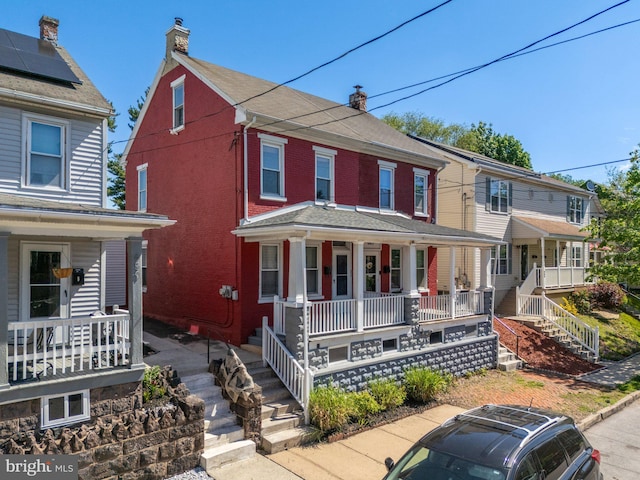 traditional style home featuring a porch, brick siding, a chimney, and stairway