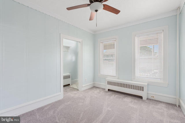 carpeted empty room featuring radiator, crown molding, ceiling fan, and baseboards