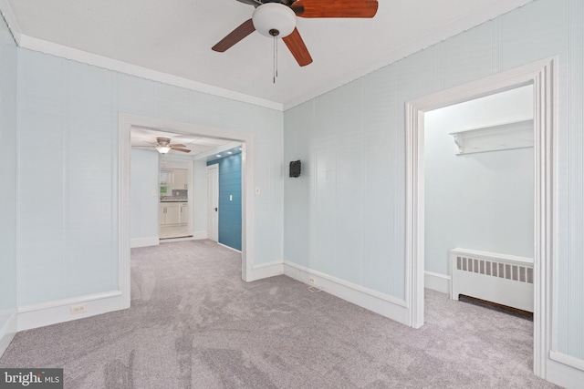 empty room with radiator heating unit, ceiling fan, carpet, crown molding, and baseboards