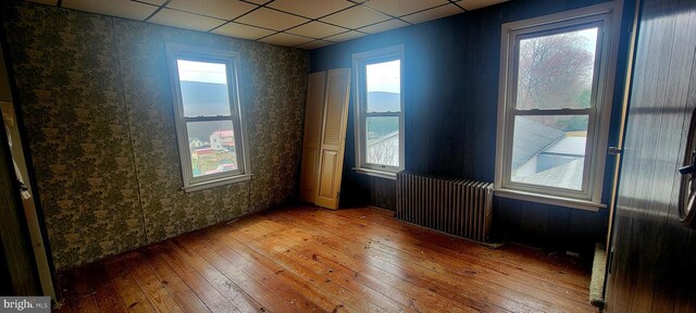 empty room with a drop ceiling, a healthy amount of sunlight, radiator heating unit, and wood-type flooring