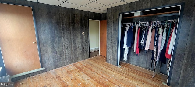 unfurnished bedroom with a paneled ceiling, a closet, wood walls, and wood finished floors
