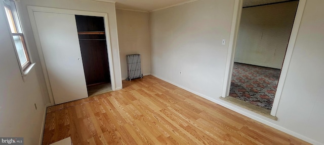 unfurnished bedroom with a closet, radiator heating unit, crown molding, baseboards, and light wood-style floors