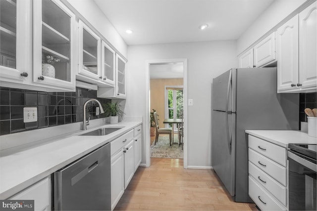 kitchen featuring dishwasher, a sink, light wood-type flooring, white cabinetry, and backsplash