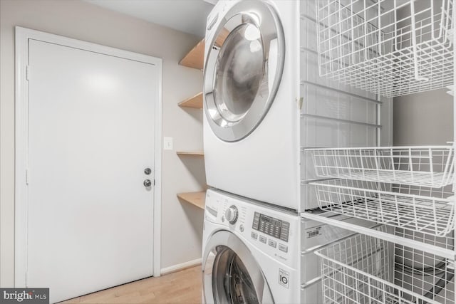 laundry room featuring stacked washer / dryer, wood finished floors, and baseboards