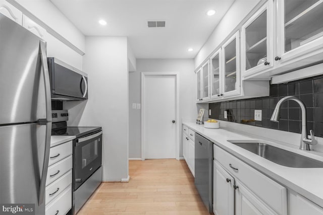 kitchen featuring appliances with stainless steel finishes, a sink, light wood finished floors, white cabinetry, and tasteful backsplash