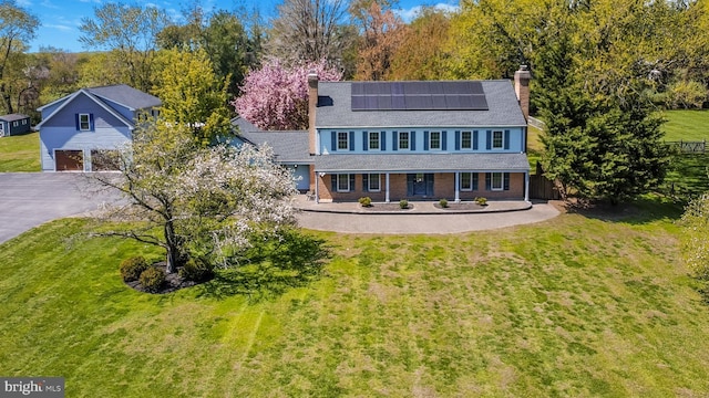 view of front of home featuring a front lawn, a chimney, driveway, and solar panels