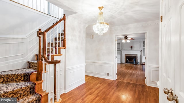 staircase featuring a decorative wall, a ceiling fan, a chandelier, wood finished floors, and ornamental molding