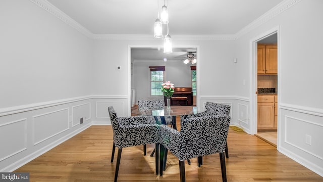 dining area with a decorative wall, a wainscoted wall, crown molding, light wood finished floors, and a ceiling fan