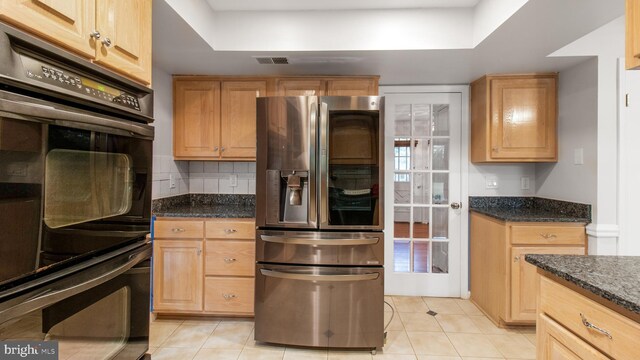 kitchen with stainless steel refrigerator with ice dispenser, light tile patterned floors, dark stone counters, backsplash, and a tray ceiling