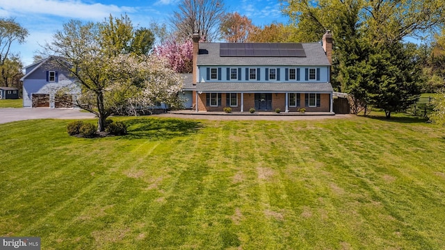 view of front of home with covered porch, roof mounted solar panels, a chimney, and driveway