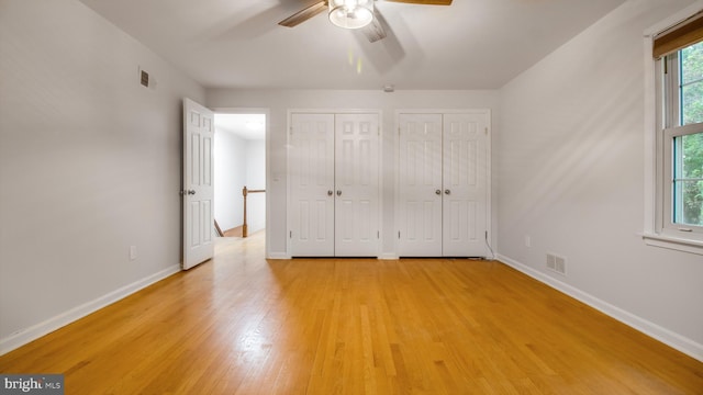 unfurnished bedroom featuring multiple closets, light wood finished floors, baseboards, and a ceiling fan