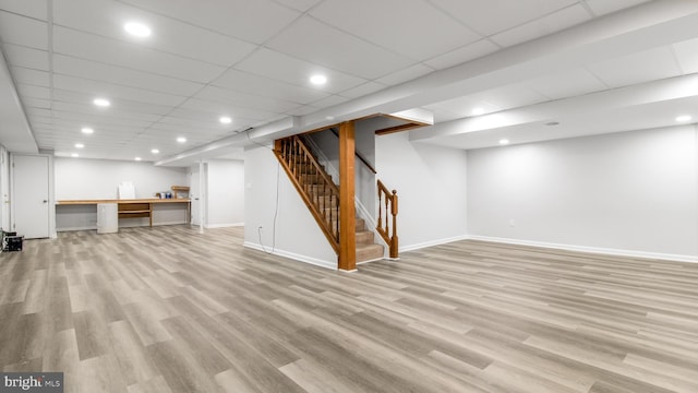 finished below grade area featuring light wood finished floors, baseboards, stairway, recessed lighting, and a drop ceiling