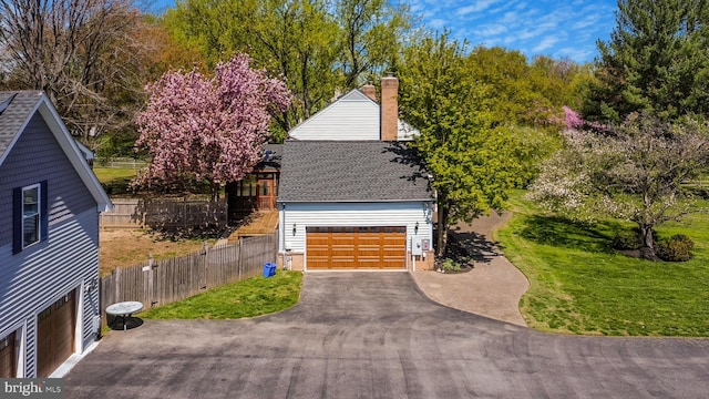 view of property exterior with roof with shingles, asphalt driveway, a chimney, and an attached garage