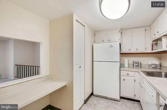 kitchen featuring white cabinets, a sink, white appliances, light countertops, and baseboards