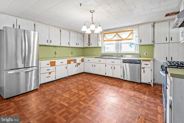 kitchen featuring appliances with stainless steel finishes, a sink, a chandelier, wall chimney exhaust hood, and hanging light fixtures