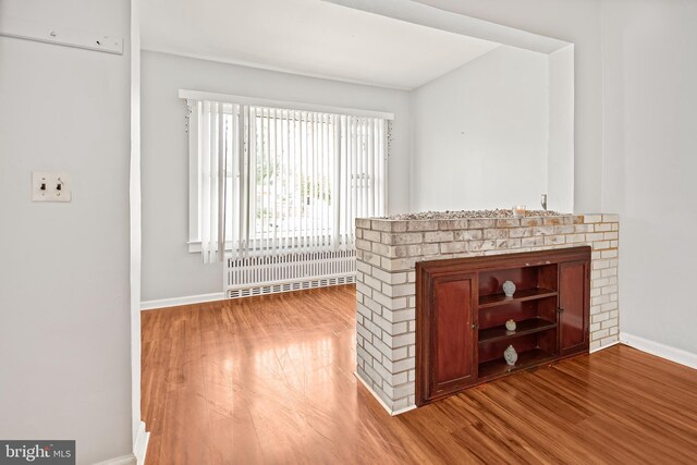 unfurnished living room featuring radiator, wood finished floors, and baseboards