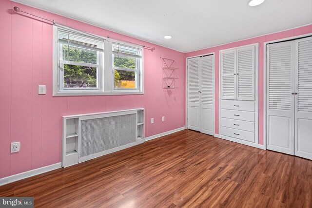 unfurnished bedroom with radiator heating unit, wood finished floors, two closets, baseboards, and recessed lighting