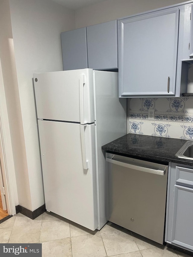 kitchen with gray cabinetry, light tile patterned floors, stainless steel dishwasher, and freestanding refrigerator