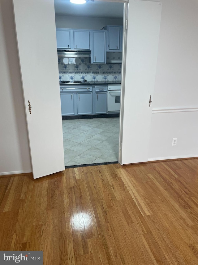 kitchen featuring dark countertops, electric stovetop, light wood-style flooring, under cabinet range hood, and white oven