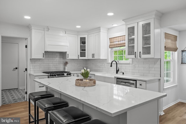 kitchen with dishwasher, a breakfast bar, a sink, white cabinetry, and premium range hood