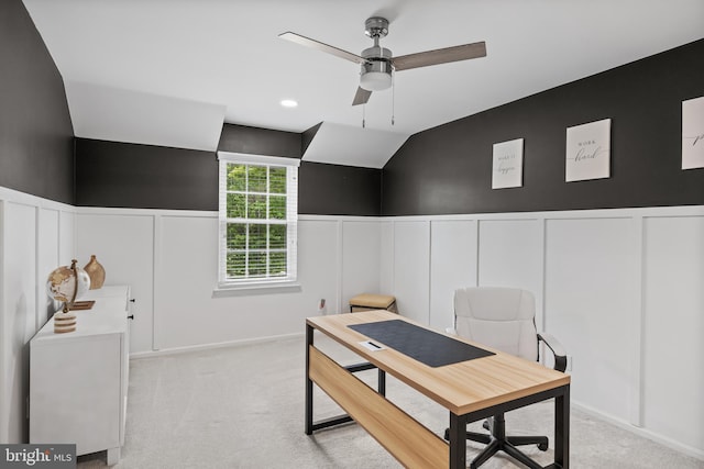 office area featuring a ceiling fan, wainscoting, a decorative wall, vaulted ceiling, and light carpet