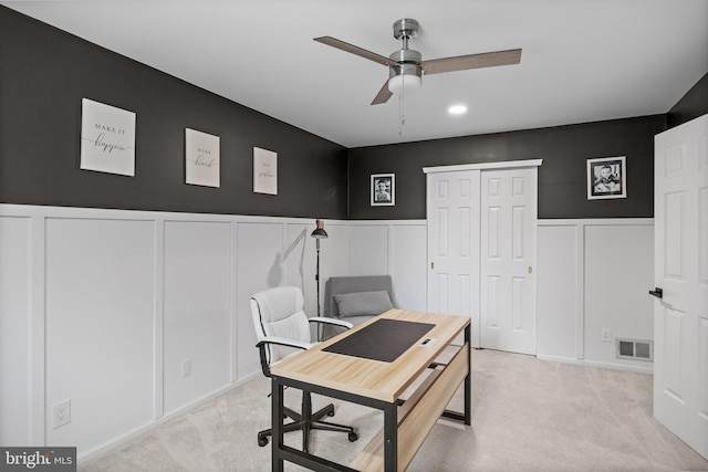 office space with a decorative wall, visible vents, ceiling fan, light carpet, and wainscoting
