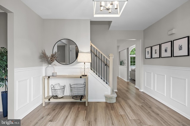 foyer entrance with stairs, a notable chandelier, a wainscoted wall, and wood finished floors